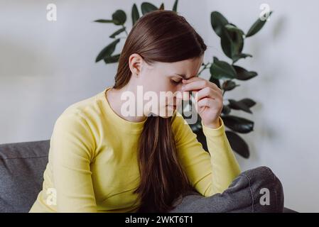 Nahaufnahme Porträt einer verärgerten traurigen jungen Frau hat Schwindel und Bewegung verschwimmen, allein auf dem Sofa im Wohnzimmer zu Hause zu sitzen. Hirnschlag oder niedriger Blutspiegel vor Stockfoto