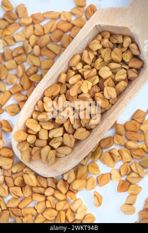 Bockshornkleesamen mit Holzlöffel auf melierter grauer Oberfläche Stockfoto