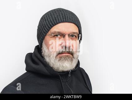 Ernster Mann mit grauem Bart und Schnurrbart im Winterhut. Blick in die Kamera. Weißer Hintergrund Stockfoto