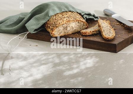 Geschnittenes Brot auf Holzbrett in Leinentasche, frische Kräuter und rostfreies Destilliermesser. Küchenästhetisches Konzept Stockfoto