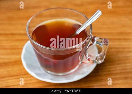 Schwarzer Tee in Glasbecher. Eine Glasschale schwarzen Tees auf einem Holztisch. Blick von oben auf eine Glasschale aromatischen heißen Tees, die auf einer Untertasse auf dem Tisch in der Cafeteria steht Stockfoto