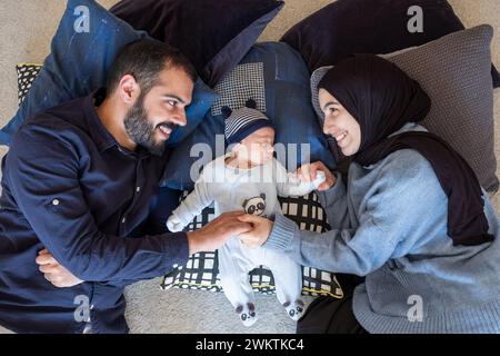 Arabisch-muslimische Eltern teilen einen zärtlichen Moment mit ihrer neugeborenen Tochter und strahlen Liebe und Freude in ihrem Zuhause aus. Stockfoto