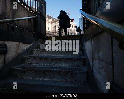 Ein flacher Blick auf das Gebäude der Bank of England in der City of London, Großbritannien, eingerahmt von der Steintreppe eines Eingangs der Bank Station. Die Union Jack (Union Flag) wird von einem Fahnenmast auf dem Dach des historischen Hauptquartiers in der Threadneedle Street aus gesehen. Stockfoto