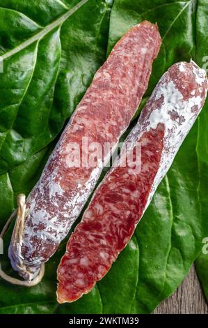 Salamiwurst. Frische Hälften eines großen Stücks Wurst auf einem Schneidebrett vor grünem Hintergrund. Schweinefleisch und Rindfleisch. Essen. Stockfoto