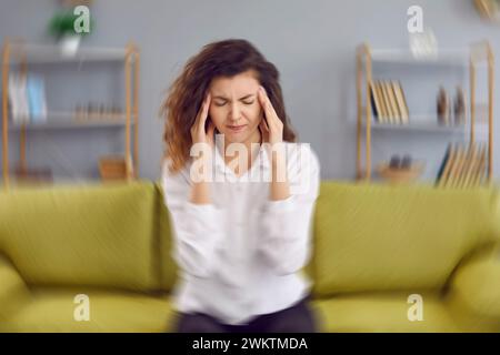 Frau, die zu Hause auf der Couch sitzt und ein schwindelerregendes Gefühl in ihrem Kopf spürt Stockfoto