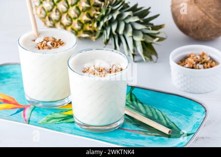 Portionen erfrischender Ananas-Kokos-Protein-Smoothies mit Granola. Stockfoto