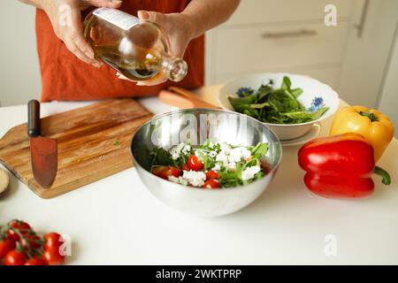 Weibliche Chefin in einer Uniform gießt Olivenöl aus einer Flasche. Kaukasische Bloggerin, die erklärt, wie man ein Gericht kocht Stockfoto