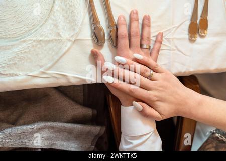 Augsburg, Bayern, Deutschland - 19. Januar 2024: Braut und Bräutigam halten ihre Hände mit den Eheringen aufeinander an einem festlich geschmückten Tisch Stockfoto