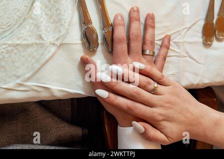 Augsburg, Bayern, Deutschland - 19. Januar 2024: Braut und Bräutigam halten ihre Hände mit den Eheringen aufeinander an einem festlich geschmückten Tisch Stockfoto