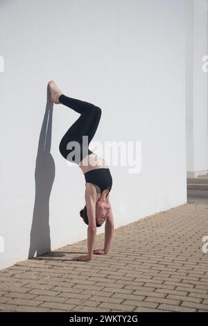 Eine Frau, die einen Handstand gegen eine weiße Wand macht, die Kernkraft, Schatten Stockfoto