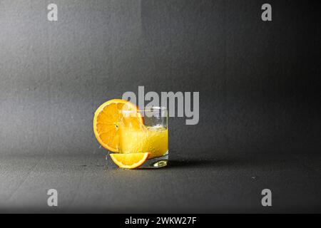 Glasbecher mit wunderbar verschüttetem Saft und Orange auf schwarzem Hintergrund. Stockfoto