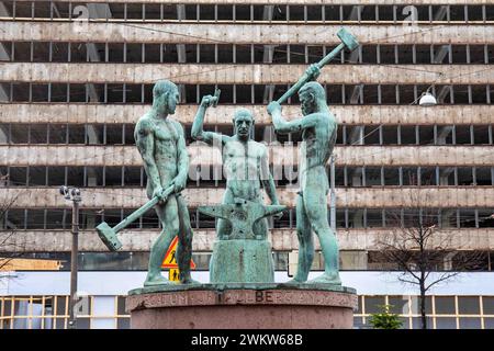 Kolmen sepän patsas, die Skulptur der drei Smiths, mit einem Bürogebäude des Aktian Talo im Hintergrund in Helsinki, Finnland Stockfoto