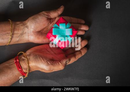 Nahaufnahme von indischen Frauenhänden, die eine kleine Geschenkbox auf schwarzem Hintergrund halten. Stockfoto