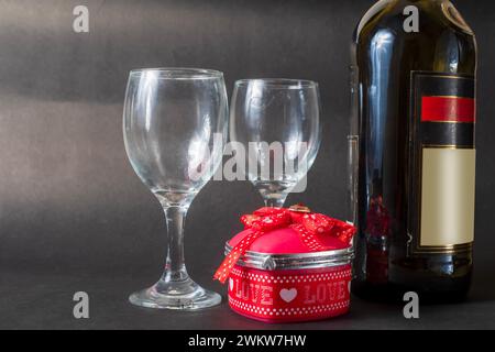 Valentinstag: Rote Geschenkbox mit roter Schleife und Weinflasche mit zwei Weingläsern auf schwarzem Hintergrund Stockfoto