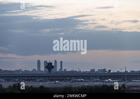 Panoramablick auf das Terminal T4 des Flughafens Madrid Barajas in der Abenddämmerung, mit der Skyline der Stadt und ihren vier Wolkenkratzern im Hintergrund. Stockfoto