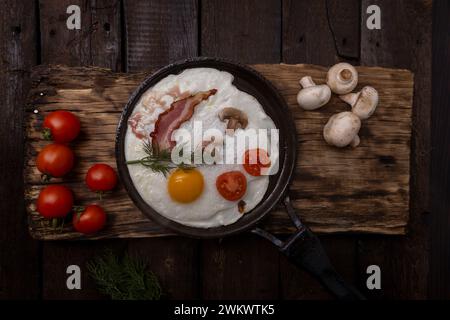 Spiegeleier mit Speck und Gemüse in gusseiserner Pfanne, auf alten dunklen Holztischhintergrund, Stockfoto