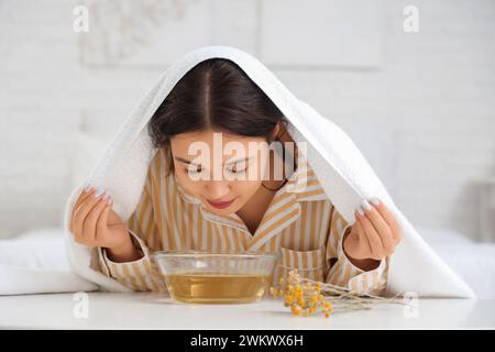 Junge asiatische Frau, die am Tisch im Schlafzimmer Dampf einatmet Stockfoto