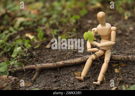 Hölzerne Menschenfigur mit jungen grünen Sämlingen auf dem Boden draußen, Platz für Text Stockfoto