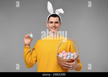 Osterfeier. Hübscher junger Mann mit Hasenohren und bemalten Eiern auf grauem Hintergrund Stockfoto