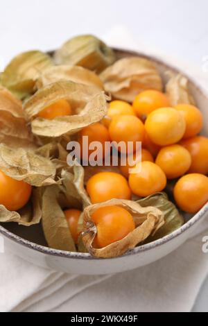 Reife Physalis-Früchte mit Kelchen in Schüssel auf weißem Tisch, Großaufnahme Stockfoto