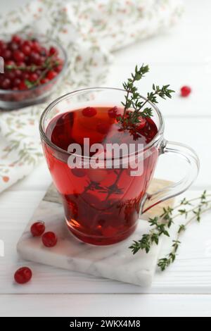 Leckerer heißer Preiselbeertee mit Thymian und frischen Beeren in Glasbecher auf weißem Holztisch Stockfoto