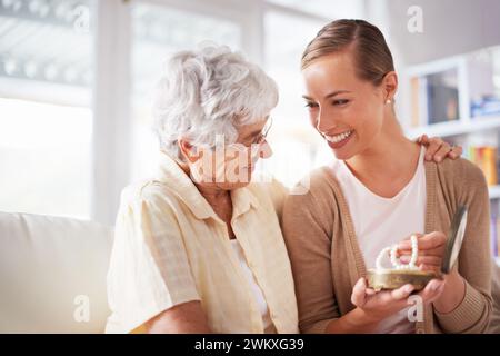 Glücklich, Halskette und ältere Mutter mit Frau als Geschenk, Geschenk und Überraschung im Wohnzimmer. Familie, Liebe und Tochter mit Mutter, die Perlen auf dem Sofa gibt Stockfoto