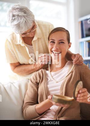 Ältere Mutter, Halskette und Porträt der Frau mit Geschenk, Geschenk und Überraschung im Wohnzimmer. Familie, Liebe und glückliche Tochter mit Mutter, die Perlen schenkt Stockfoto