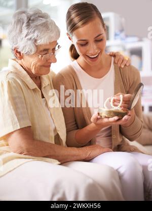 Familie, Halskette und ältere Mutter mit Frau als Geschenk, Geschenk und Überraschung im Wohnzimmer. Zuhause, Perlen und glückliche Tochter mit Mutter, die das Erbstück gibt Stockfoto