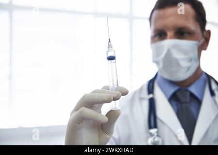 Arzt, Spritze und Impfstoff-Injektion mit Nadel zur Krankheitsbehandlung bei Influenzavirus, Antibiotika oder im Gesundheitswesen. Männliche Person, Gesichtsmaske und Stockfoto