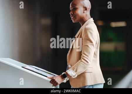 Elegante Frau steht selbstbewusst und hält eine Geschäftsrede. Sie strahlt Professionalität mit einem stylischen Blazer und einer eleganten Kleidung aus und macht sie zu einem idealen Kleidungsstück Stockfoto