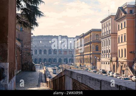 Malerische Straße in Rom, Italien. Das berühmte Kolosseum ragt in der Ferne und taucht in der Morgensonne auf. Sonnenstrahlen beleuchten das nahe gelegene b Stockfoto