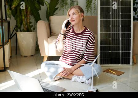 Lächelnder Manager, der Telefonanruf entgegennimmt, Kunden zu Solarpaneelen und Windturbinen berät Stockfoto