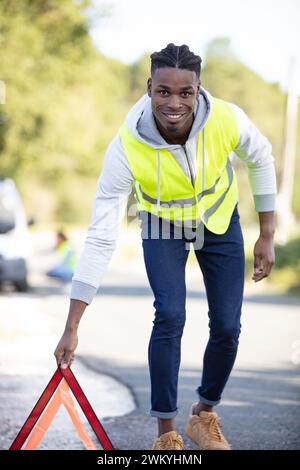 Mann in der Straßenweste, der ein Notfall-Dreieck-Schild hält Stockfoto