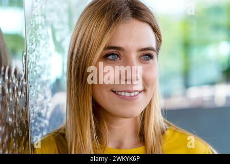 Dieses Nahaufnahme-Bild zeigt den fesselnden Blick einer jungen Frau mit einem warmen Lächeln und trägt ein gelbes Oberteil, das ihren fröhlichen Ausdruck unterstreicht. Die Ba Stockfoto