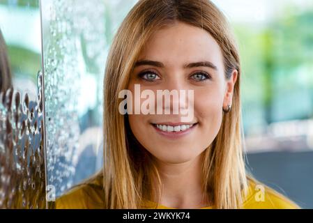 Dieses Nahaufnahme-Bild zeigt den fesselnden Blick einer jungen Frau mit einem warmen Lächeln und trägt ein gelbes Oberteil, das ihren fröhlichen Ausdruck unterstreicht. Die Ba Stockfoto