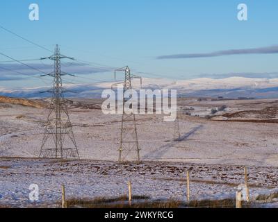 Strommasten erstrecken sich über das schneebedeckte Moorland der Shap Fells an einem hellen, sonnigen Wintertag in die Ferne. Stockfoto