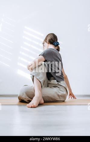 Frau in legeren Kleidern, die sitzende Twist-Yoga-Pose auf Korkmatte macht Stockfoto