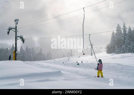 Nicht erkennbares Kind klettert auf Skiern einen Schlepplift, Blick von hinten Stockfoto