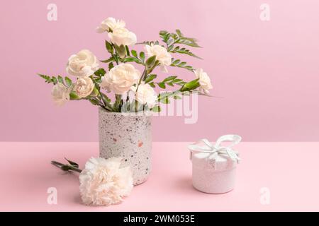 Blumenstrauß aus weißen Nelken in einer Vase und einer Geschenkbox auf rosa Hintergrund. Stockfoto