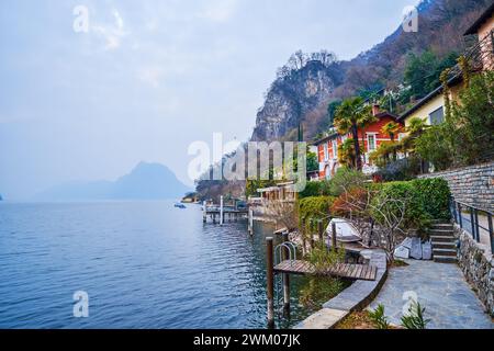 Gebäude am See am felsigen Ufer des Luganer Sees entlang des Olive Tree Trail, Lugano, Schweiz Stockfoto