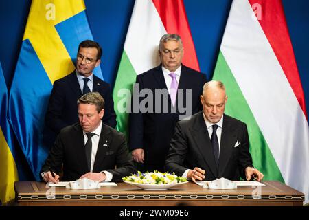 Budapest, Ungarn. Februar 2024. Göran Martensson (l), Generaldirektor der schwedischen Wehrmaterialverwaltung, und ungarischer Verteidigungsminister Kristof Szalay-Bobrovniczky unterzeichnen einen Vertrag während einer gemeinsamen Pressekonferenz in Budapest. Im Hintergrund stehen der schwedische Premierminister Ulf Kristersson (l) und der ungarische Premierminister Viktor Orban. Kurz vor der erwarteten Zustimmung Ungarns zum NATO-Beitritt Schwedens haben sich die beiden Länder auf ein umfassendes Rüstungsabkommen geeinigt. Quelle: Marton Monus/dpa/Alamy Live News Stockfoto