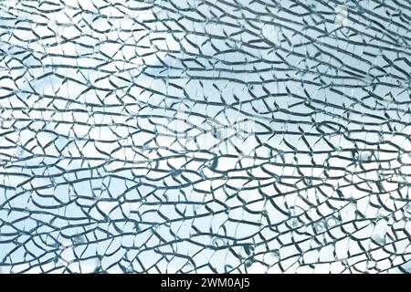 Im zersplitterten Glas bilden sich komplizierte Muster, die ein komplexes Rissgewebe erzeugen. Die lichtdurchlässigen Fragmente reflektieren das Licht und zeigen eine zarte, aber chaotische Schönheit. Die Textur von Glasbruch vor blauem Himmel. Stockfoto