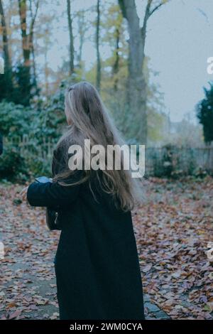 Frau in schwarzem Fell inmitten von Herbstblättern, mit Bäumen im Hintergrund Stockfoto