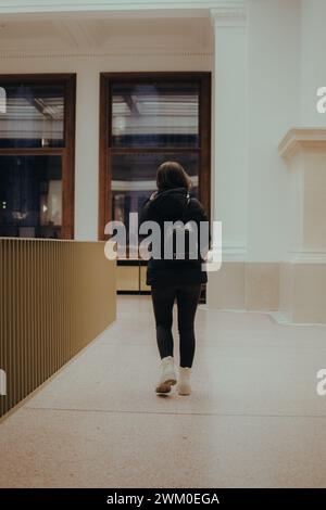Eine Frau in schwarzem Mantel, die an zwei Fenstern in einem Flur vorbeischlendert Stockfoto