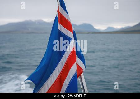 Islandflagge auf dem fahrenden Boot im Meer mit einer wunderschönen Landschaft aus Bergen unter dem Schnee, dem Land des Feuers und des Eises. Reiseziel im Geheimen Stockfoto