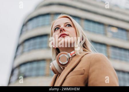 Aufmerksame Frau mit schnurlosen Kopfhörern vor dem Gebäude Stockfoto