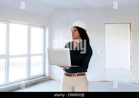 Architekt trägt einen Schutzhelm und steht mit Laptop vor Ort Stockfoto