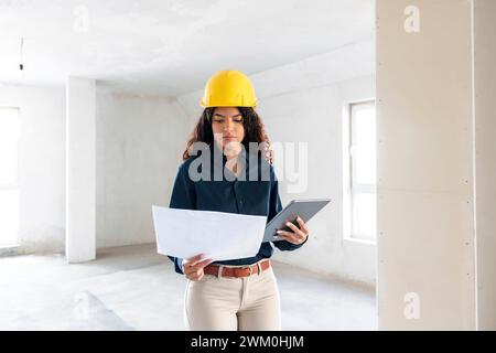 Architekt trägt gelben Schutzhelm und untersucht den Entwurf mit Tablet-PC vor Ort Stockfoto