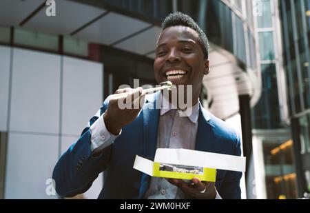 Glücklicher reifer Geschäftsmann, der Sushi vor den Gebäuden genießt Stockfoto