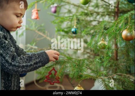 Süßer Junge, der zu Hause den Weihnachtsbaum dekoriert Stockfoto